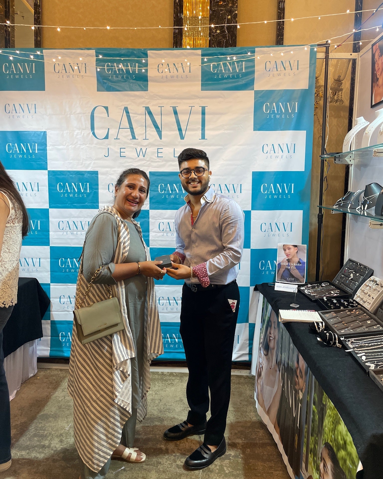 Two people standing in front of a Canvi Jewelry display with a branded backdrop.